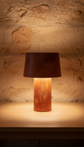 A terracotta table lamp with a sleek, modern design, perfectly centered on a wooden surface. The lamp is lit to showcase...